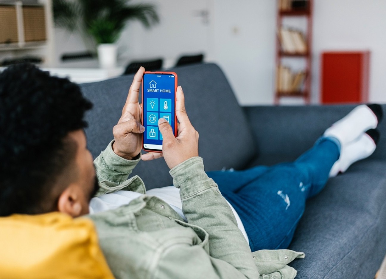 Bühnenbild Ratgeber Smart Home Ein Jugendlicher liegt auf dem Sofa und hält sein Mobiltelefon in der Hand.