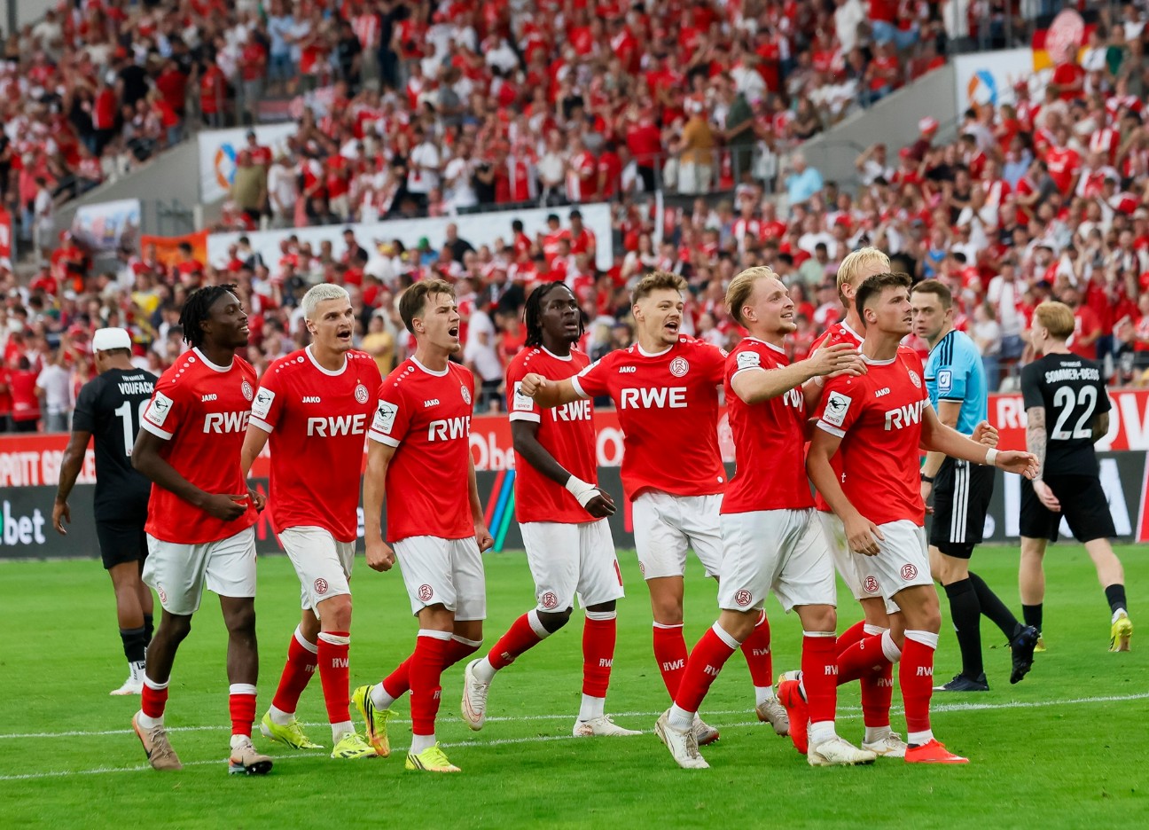 Fußballspieler von Rot-Weiss Essen feiern gemeinsam auf dem Spielfeld vor einer voll besetzten Tribüne.