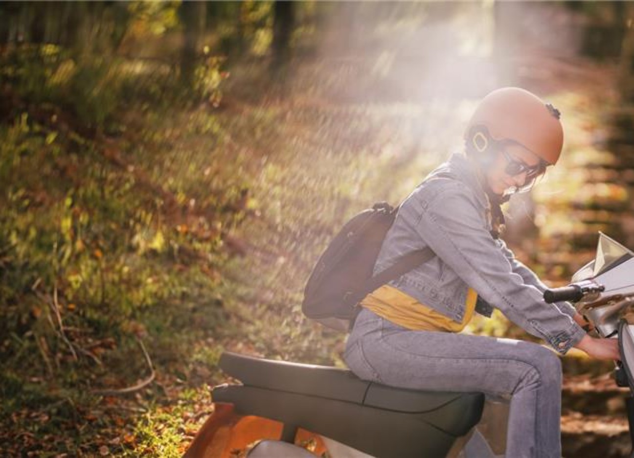 Eine junge Frau mit Helm fährt auf einem Moped eine Wiese entlang.