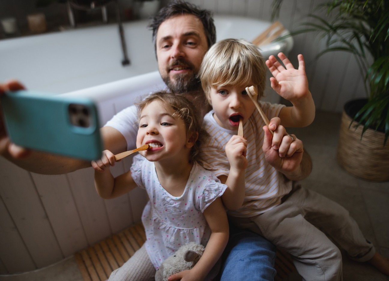 Ein Vater nimmt mit seiner Tochter und seinem Sohn ein Selfie auf, während sie beide am Zähne putzen sind.