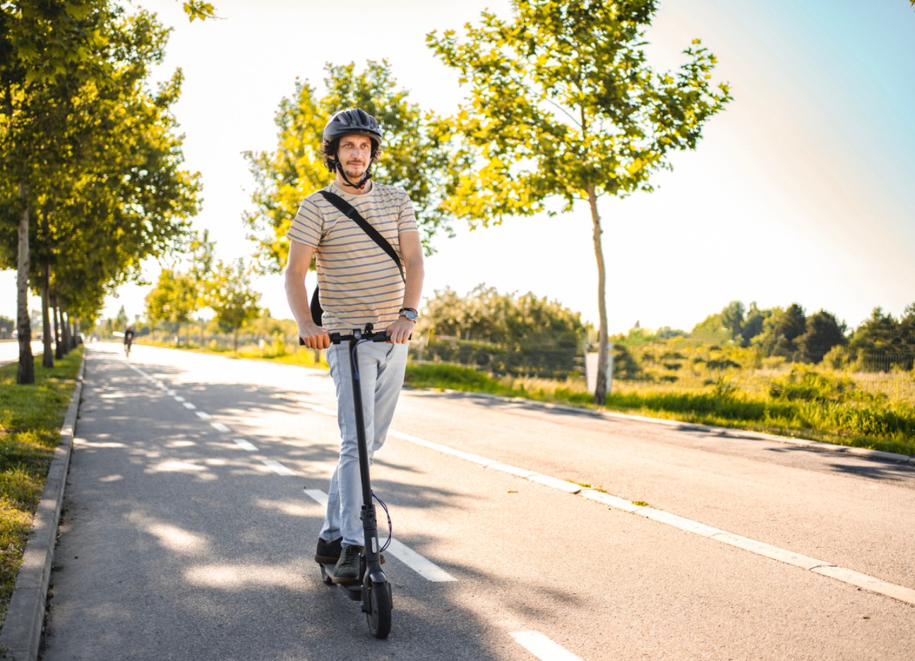Mann trägt Schutzhelm beim Fahren mit seinem E-Scooter. Mann trägt Schutzhelm beim Fahren mit seinem E-Scooter.