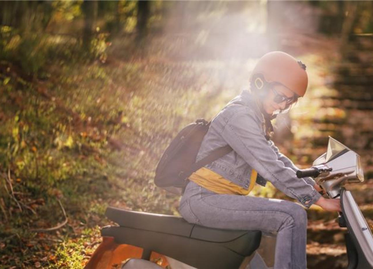 Eine junge Frau mit Helm fährt auf einem Moped eine Wiese entlang.