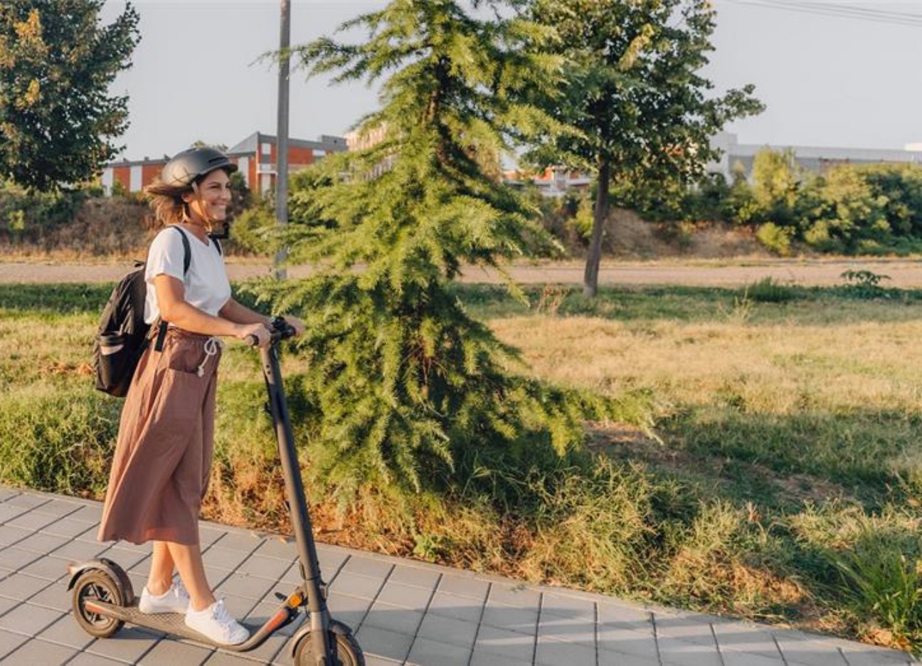 Eine junge Frau mit Helm fährt mit einem E-Scooter durch die Stadt.