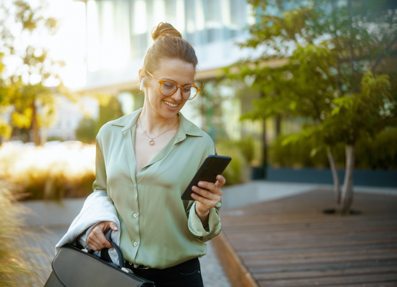 Eine junge Frau verlässt Bürogebäude und schaut glücklich auf ihr Telefon.