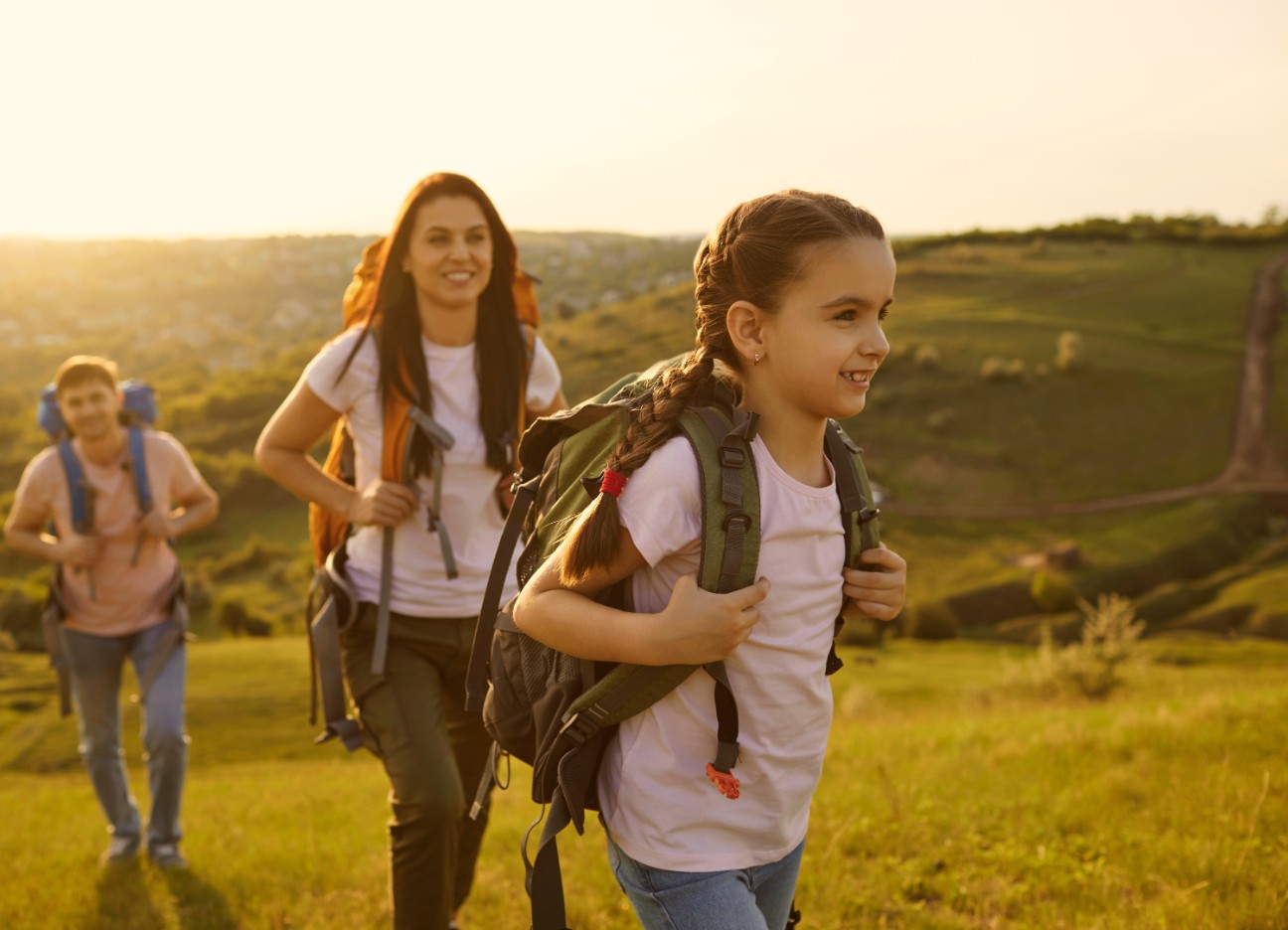 Eine junge Familie geht im Sonnenschein wandern. Die junge Tochter steht im Vordergrund.