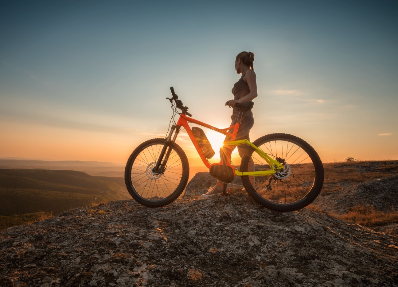 Bühnenbild Ratgeber E-Bike Eine Frau sitzt auf ihrem E-Bike auf einem Berg im Sonnenuntergang.