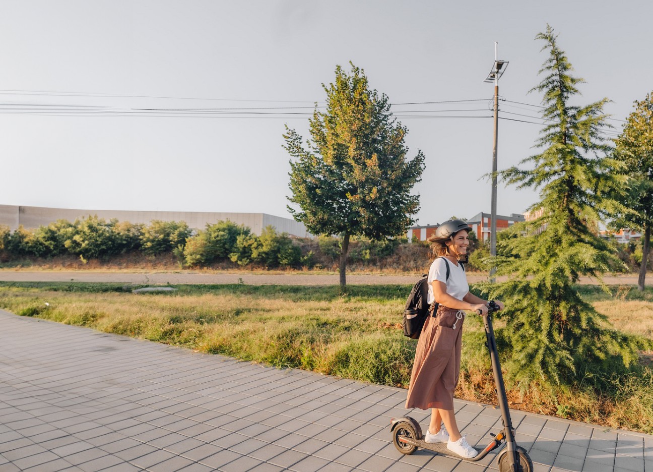 Eine junge Frau mit Helm fährt mit einem E-Scooter einen Grünstreifen entlang.