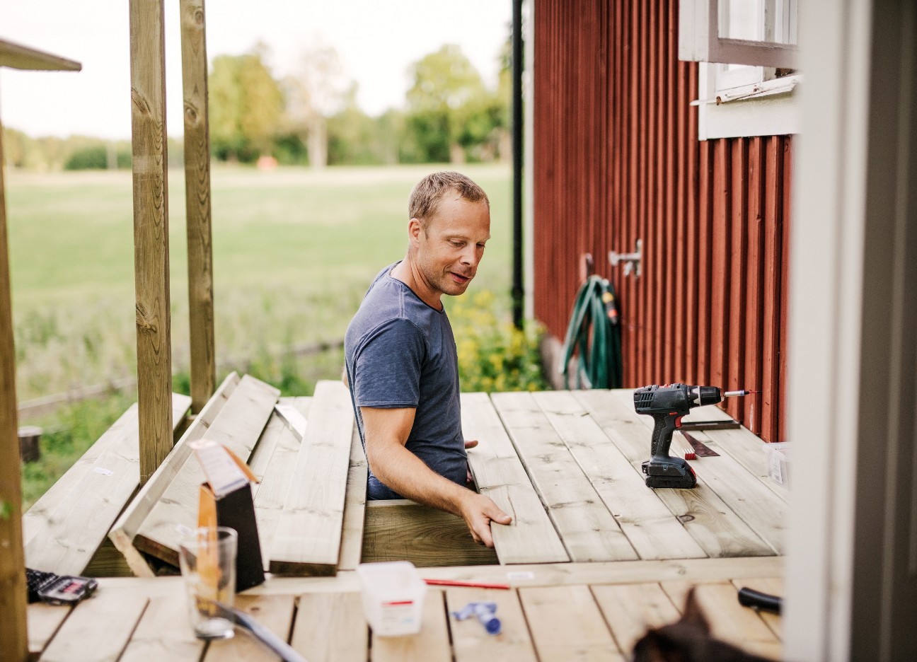 Ein Mann arbeitet an der Holzterrasse eines roten Schwedenhauses. 