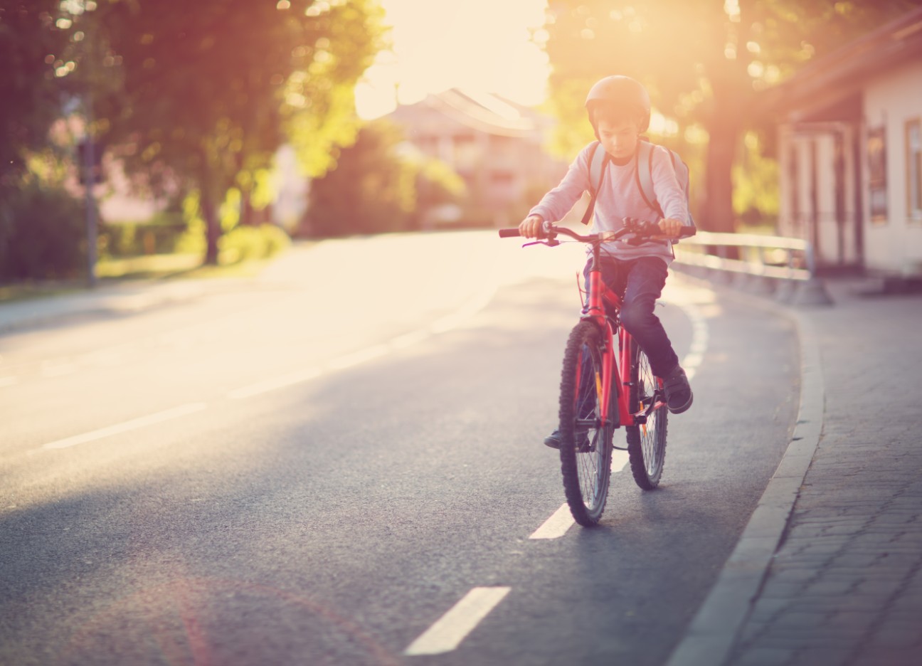 Bühnenbild Ratgeber Einschulung Schulweg Ein junges Kind fährt mit seinem Fahrrad den Fahrradstreifen auf einer Straße entlang.