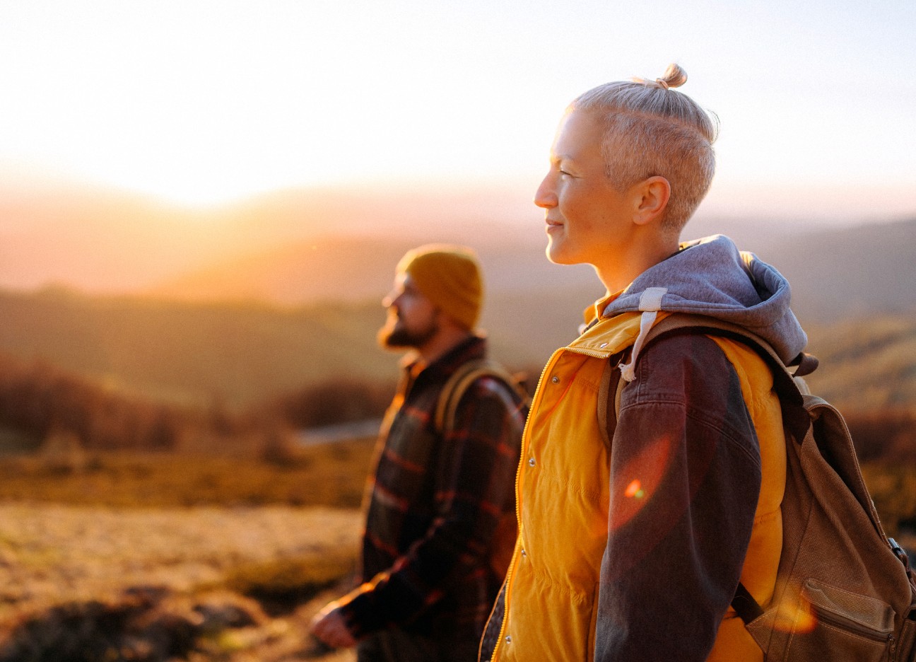 Eine Frau und ein Mann stehen in goldenem Licht in der Landschaft und schauen nach links.