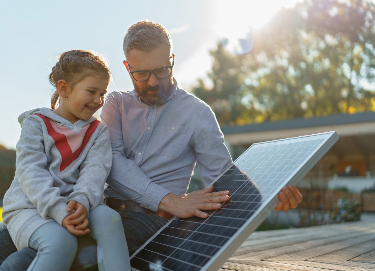 Vater zeigt seiner kleinen Tochter ein Solarpaneel für eine Photovoltaik-Anlage Vater zeigt seiner kleinen Tochter ein Solarpaneel für eine Photovoltaik-Anlage