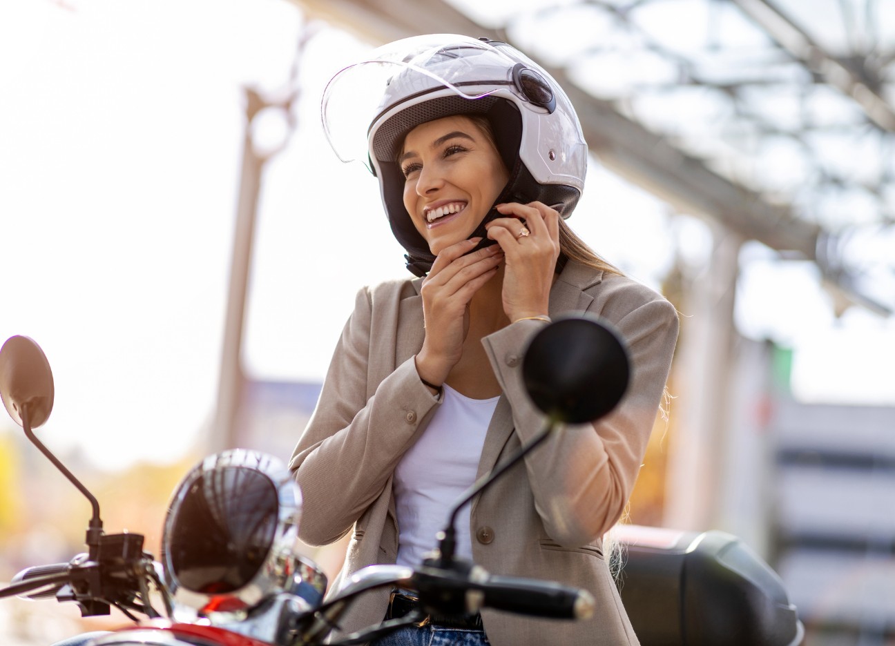 Eine junge Frau sitzt im Sonnenschein auf ihrem Moped-Roller und startet diesen.
