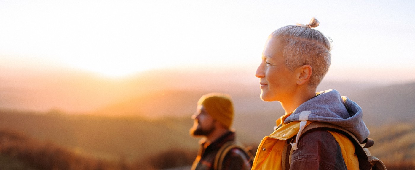 Eine Frau und ein Mann stehen in goldenem Licht in der Landschaft und schauen nach links.