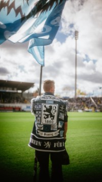 Fan des TSV 1860 schwenkt Fahne des TSV 1860 auf dem Spielfeld