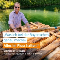 Wolfgang Fischinger auf einem Floß; Schriftzug: "Was ich bei der Bayerischen genau mache? Alles im Fluss halten!"