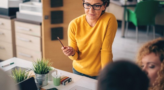 Frau im gelben Pullover steht in einer Runde von Menschen und erklärt Jahresbericht
