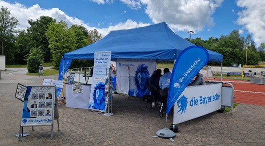 Messestand der Bayerischen bei einer Sportveranstaltung mit blauem Pavillon und Beachflags.