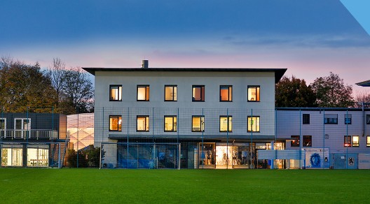 Gebäude mit großen Fenstern und einem Fußballfeld im Vordergrund bei Dämmerung. Gebäude mit großen Fenstern und einem Fußballfeld im Vordergrund bei Dämmerung.