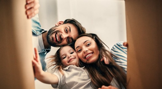 Eine lachende Familie sieht von oben in einen Karton