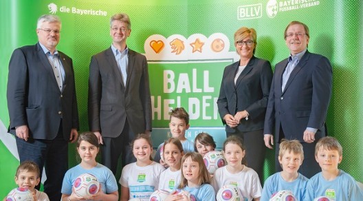 Gruppe von Erwachsenen und Kindern vor "Ball Helden"-Banner, Kinder halten Fußbälle. Gruppe von Erwachsenen und Kindern vor "Ball Helden"-Banner, Kinder halten Fußbälle.