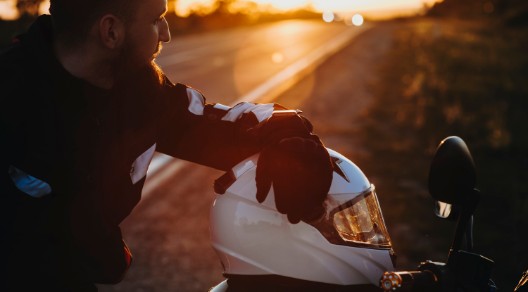 Motorradfahrer macht während einer Fahrt bei Sonnenuntergang eine Pause. Der Helm liegt auf dem Motorrad. Motorradfahrer macht während einer Fahrt bei Sonnenuntergang eine Pause. Der Helm liegt auf dem Motorrad.