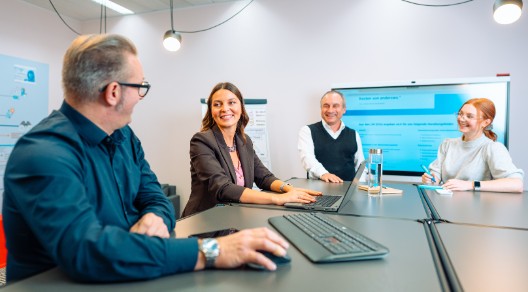 Mehrere Kolleginnen und Kollegen in einem Besprechungsraum schauen gemeinsam auf einen Laptop 