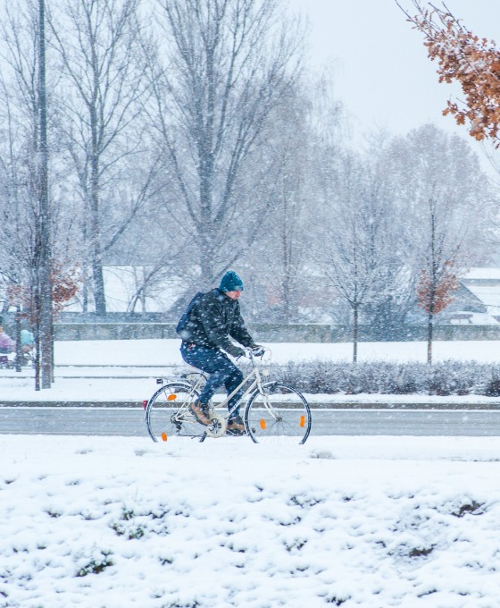 Ein Mann fährt im Schnee und durch einen leichten Schneesturm sein Fahrrad. 