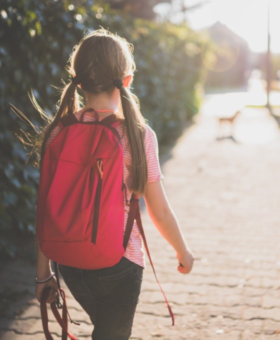 Ein junges Mädchen, fotografiert von hinten, läuft mit ihrem Rucksack eine Straße entlang.