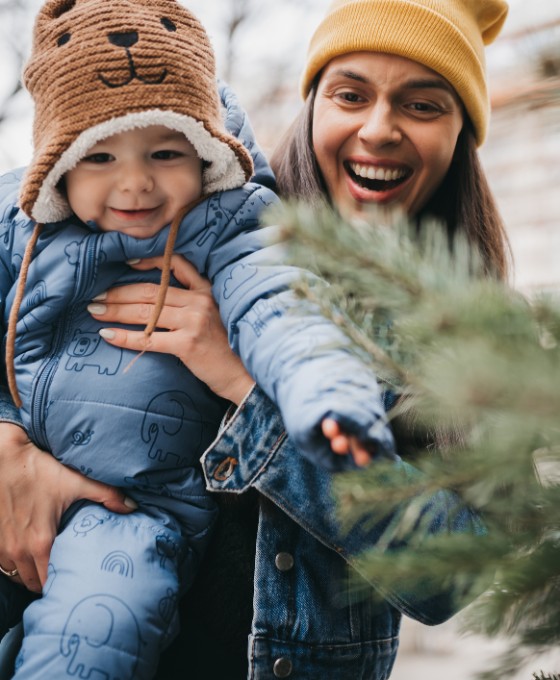 Glückliche Frau hält ihr Baby vor einem Tannenbaum.