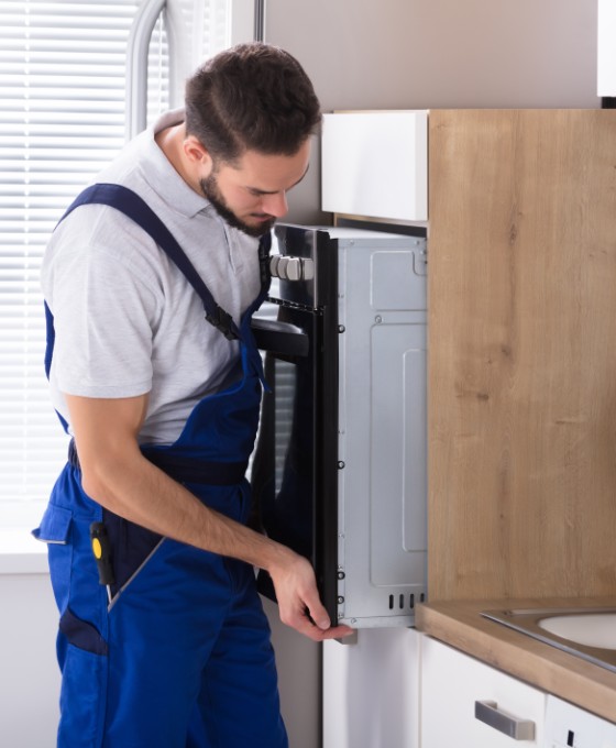 Ein Elektriker steht in einer Küche und untersucht einen Ofen, den er zuvor leicht aus dem Küchenschrank gezogen hat.