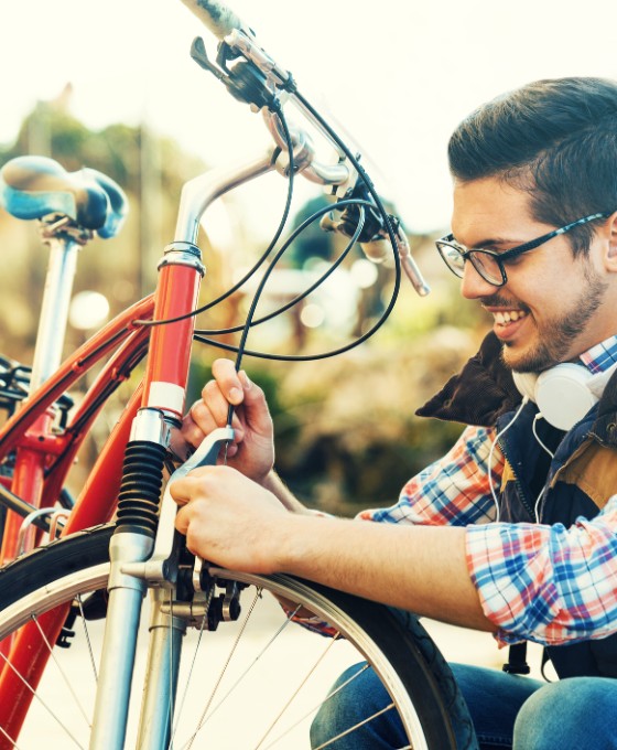 Eine Person repariert im Freien ein rotes Fahrrad und verwendet dabei ein Werkzeug an der Vordergabel.