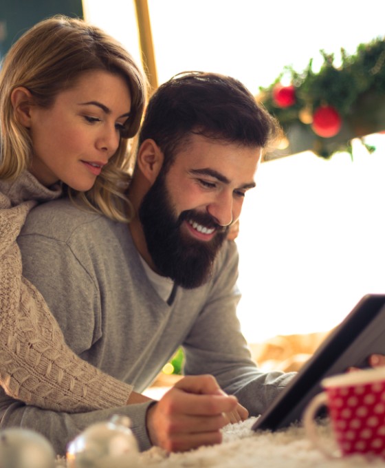 Ein Pärchen schaut zusammen in ein Tablet. Die Umgebung schaut weihnachtlich aus.