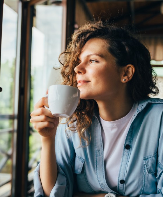 Eine junge Frau schaut aus dem Fenster, während sie einen Kaffee trinkt. 