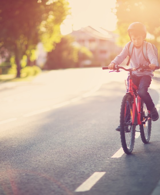 Ein junges Kind fährt mit seinem Fahrrad den Fahrradstreifen auf einer Straße entlang. 