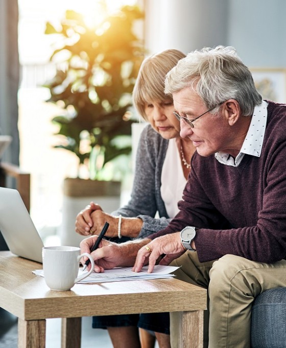 Ein älteres Ehepaar sitzt zusammen im Wohnzimmer am Laptop.