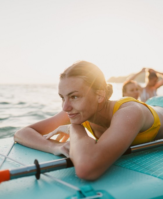 Eine junge Frau liegt auf dem Standup-Paddle-Board auf dem Wasser und schaut in die Ferne.