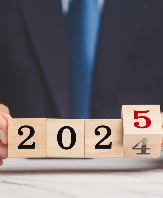 Eine Person mit Anzug hält Holzklötze mit den Zahlen 2024 und 2025 in der Hand. Die Zahl 4 wird hierbei durch eine 5 ersetzt.