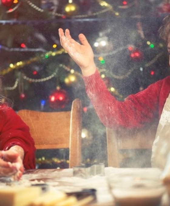 Zwei kleine Kinder backen zusammen und albern rum. Im Hintergrund ist ein Weihnachtsbaum.