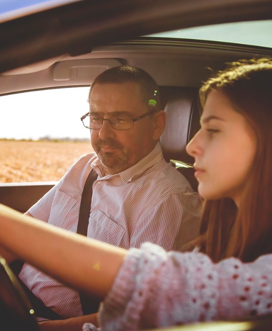 Ein junges Mädchen und ein erwachsener Mann sitzen zusammen in einem Auto. Das junge Mädchen sitzt am Steuer und lernt das Autofahren.
