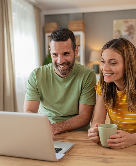 Ein Pärchen sitzt am Wohnzimmertisch und schaut gemeinsam auf einen Laptop.