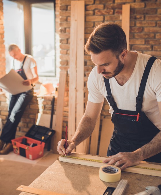 Ein Mann arbeitet auf einer Baustelle und misst ein Stück Holz ab. 