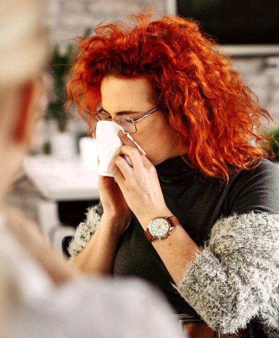 Eine Frau sitzt im Büro und putzt sich die Nase.