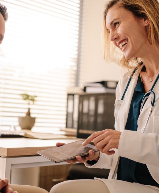 Eine Ärztin berät einen männlichen Patienten und hält ein Tablet in der Hand.