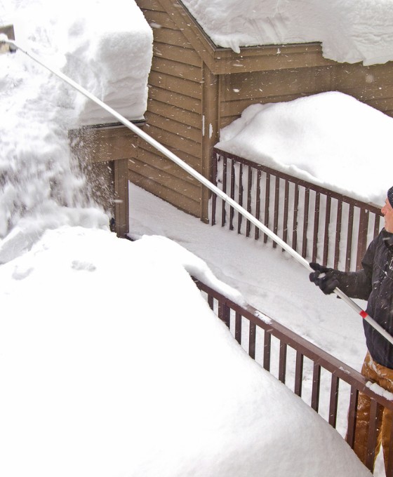 Ein Mann mit einem Schnee-Rechen entfernt Schnee vom Dach.