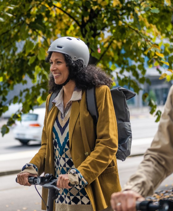 Älterer Mann fährt neben einer jüngeren Frau geschützt mit Helm E-Scooter.