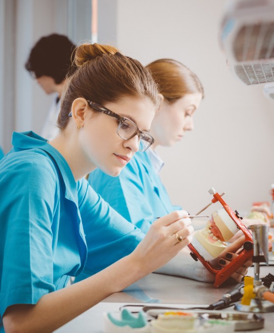 Eine Zahnarzthelferin sitzt in einem Labor und arbeitet an einem Gebissmodell. 