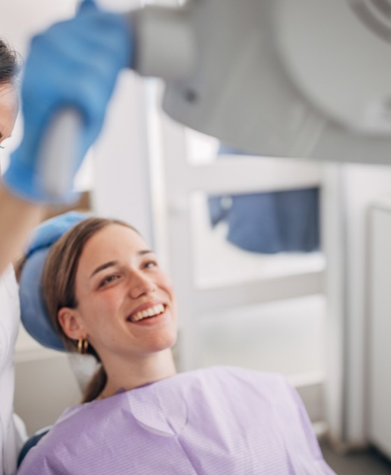 Eine junge Frau liegt auf der Zahnarztliege. Neben ihr steht eine Zahnärztin, die beiden haben einen fröhlich lachenden Gesichtsausdruck