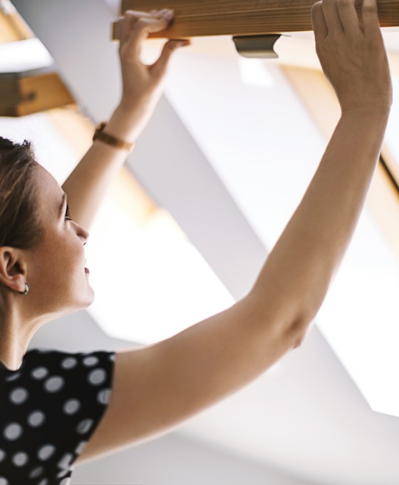 Frau öffnet Dachfenster zum Lüften, um Schimmelbildung in der Wohnung vorzubeugen.