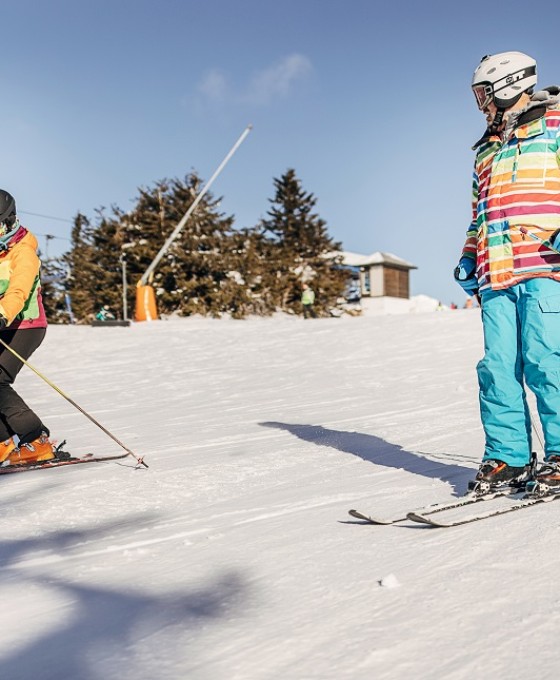 Zwei Kinder, die nebeneinander her auf einer Skipiste Ski fahren. 
