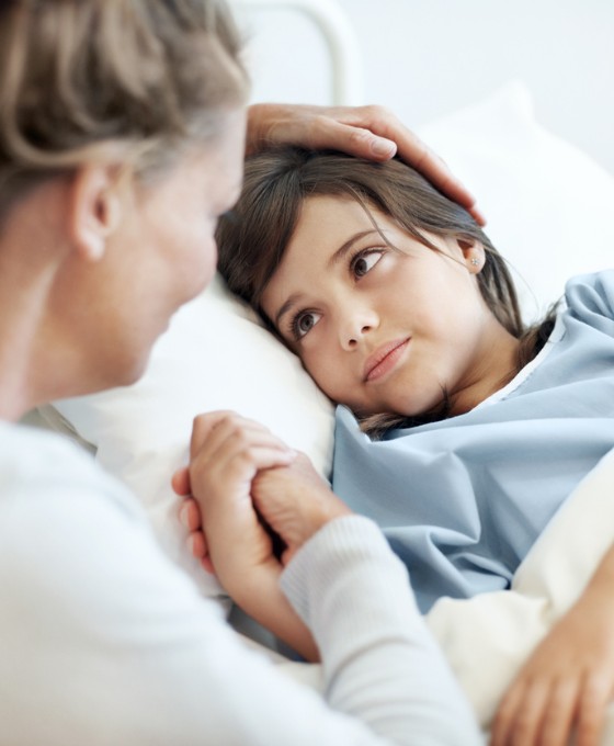 Ein kleiner Junge liegt im Krankenbett. Seine Mutter sitzt daneben und streichelt ihm den Kopf.